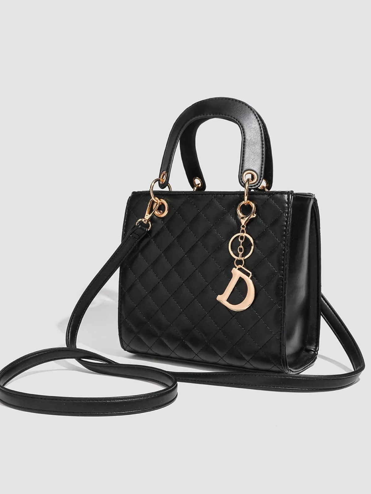 Mini black PU leather quilted top-handle handbag with a structured silhouette, gold-tone hardware, decorative pendant, and long shoulder strap.