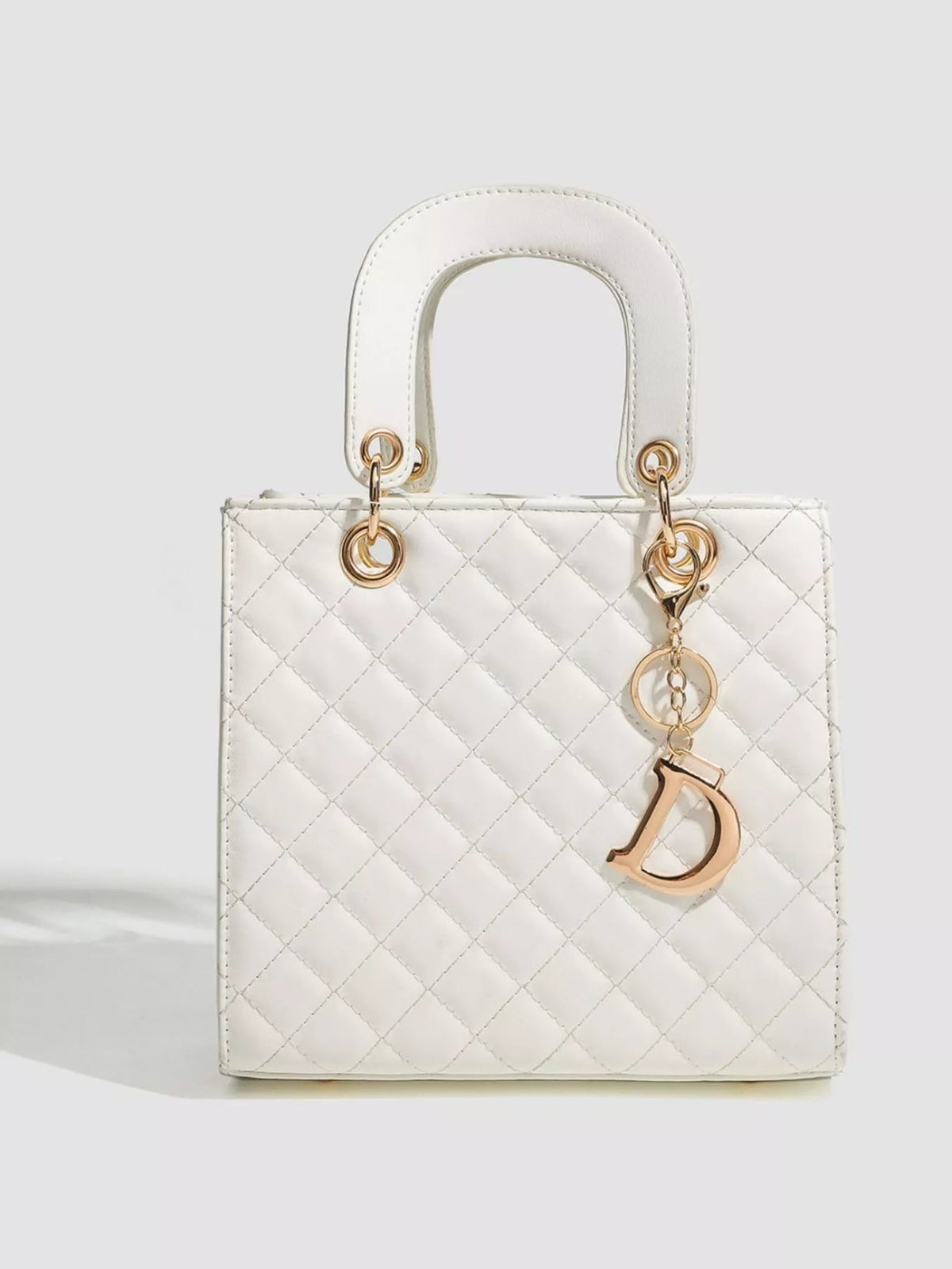 White mini quilted PU leather handbag with a structured rectangular silhouette, rounded top handles, gold-tone hardware, and a dangling letter charm.