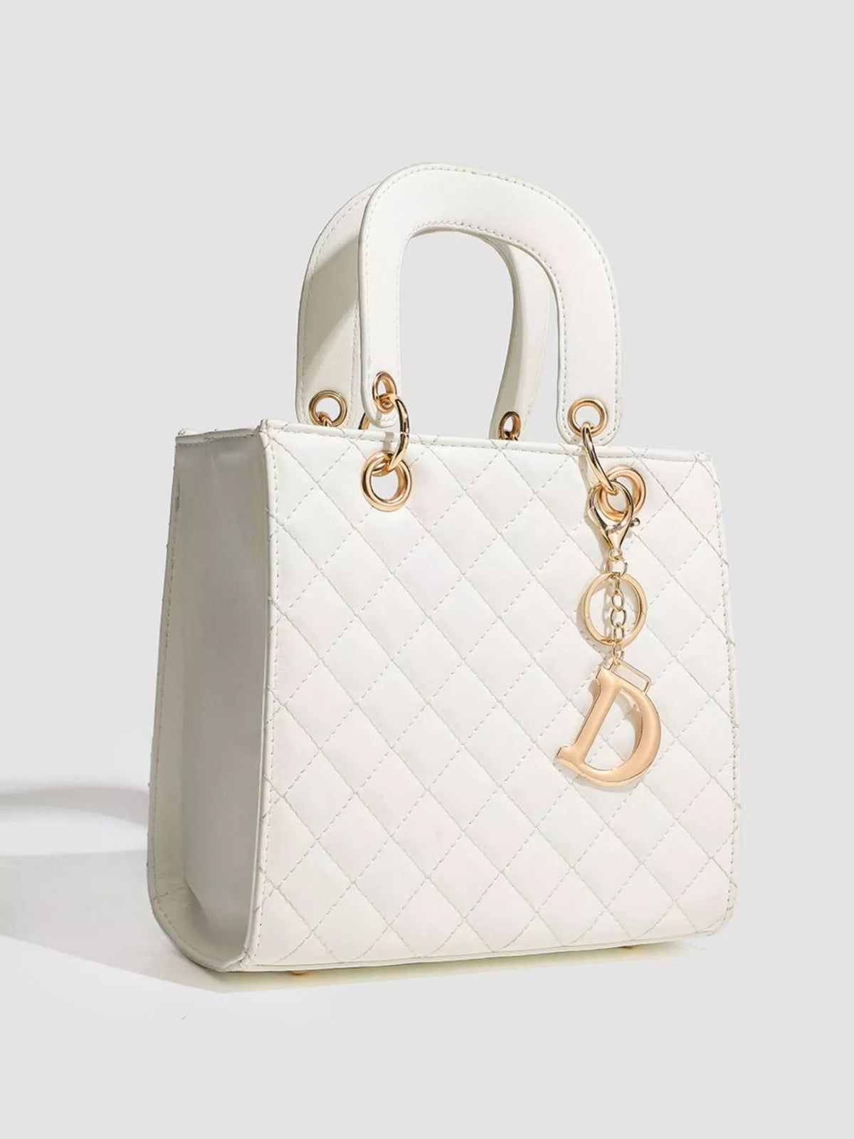 White mini PU leather quilted top handle handbag with a structured silhouette, twin handles, gold-tone ring hardware, and a hanging letter charm.