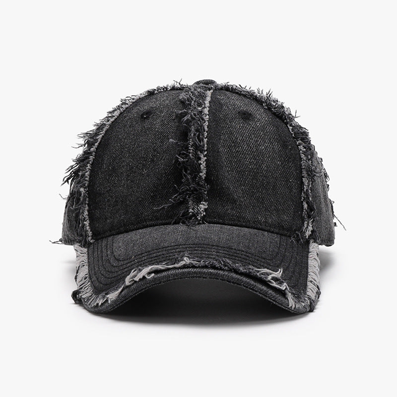 Black cotton baseball cap with a six-panel crown, curved brim, ventilation eyelets, tonal stitching, and distinctive raw frayed hems along the seams.