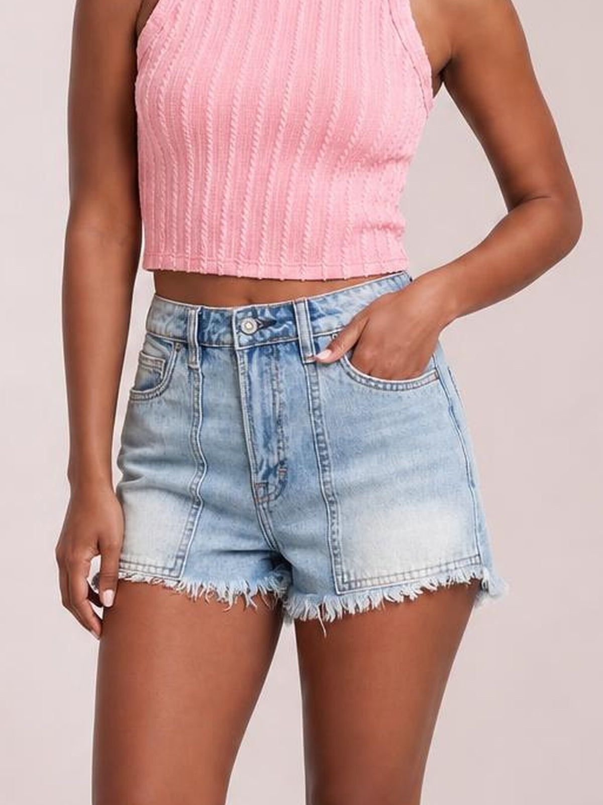 A model wears light blue washed denim shorts with a high-rise silhouette, front pockets, belt loops, button closure, and frayed raw hems.
