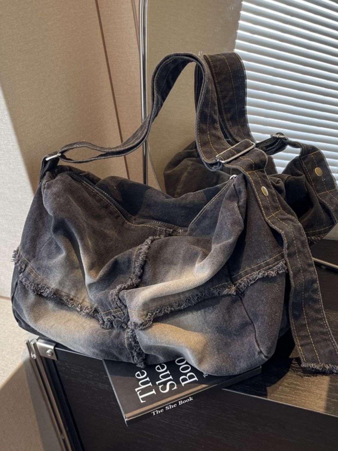 Large gradient denim crossbody bag with a relaxed slouchy silhouette, long adjustable strap, contrast stitching, and distinctive raw hem detailing.
