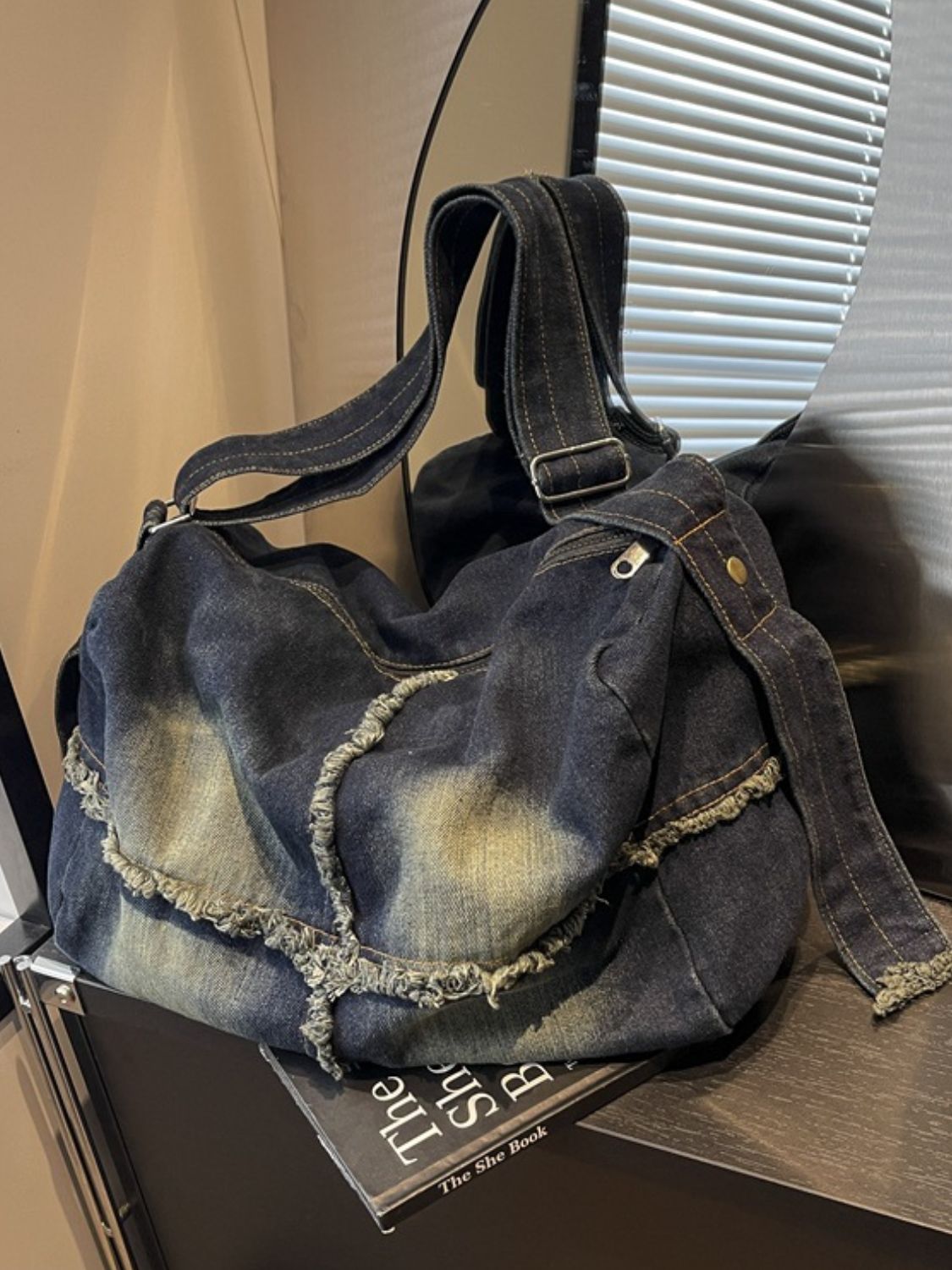 Large dark denim crossbody bag with a slouched silhouette, gradient wash, raw fringed hem detailing, contrast stitching, and a long adjustable strap.