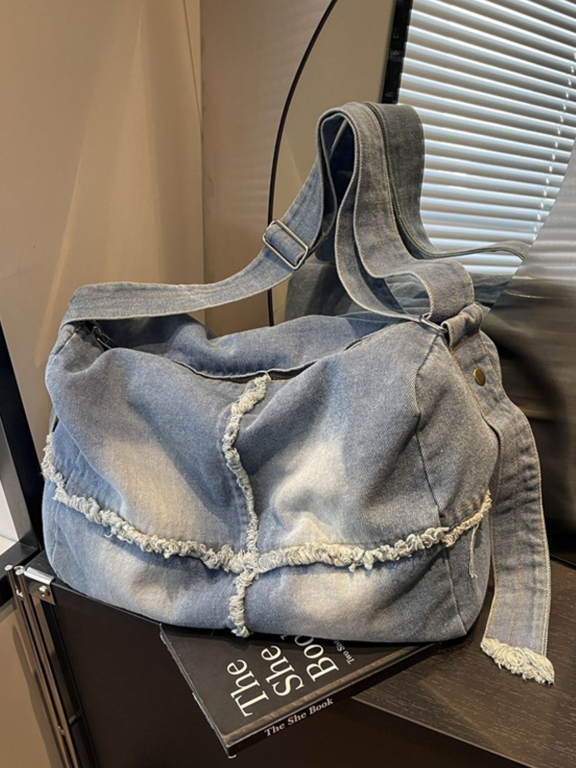 Large light blue gradient denim crossbody bag with a relaxed slouched silhouette, raw frayed hem detailing, and a long adjustable shoulder strap.