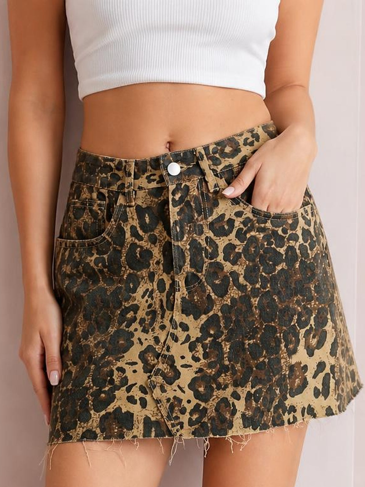 Model wearing a leopard-print denim skirt with a brown and black pattern, button closure, front pockets, and a raw frayed hem.