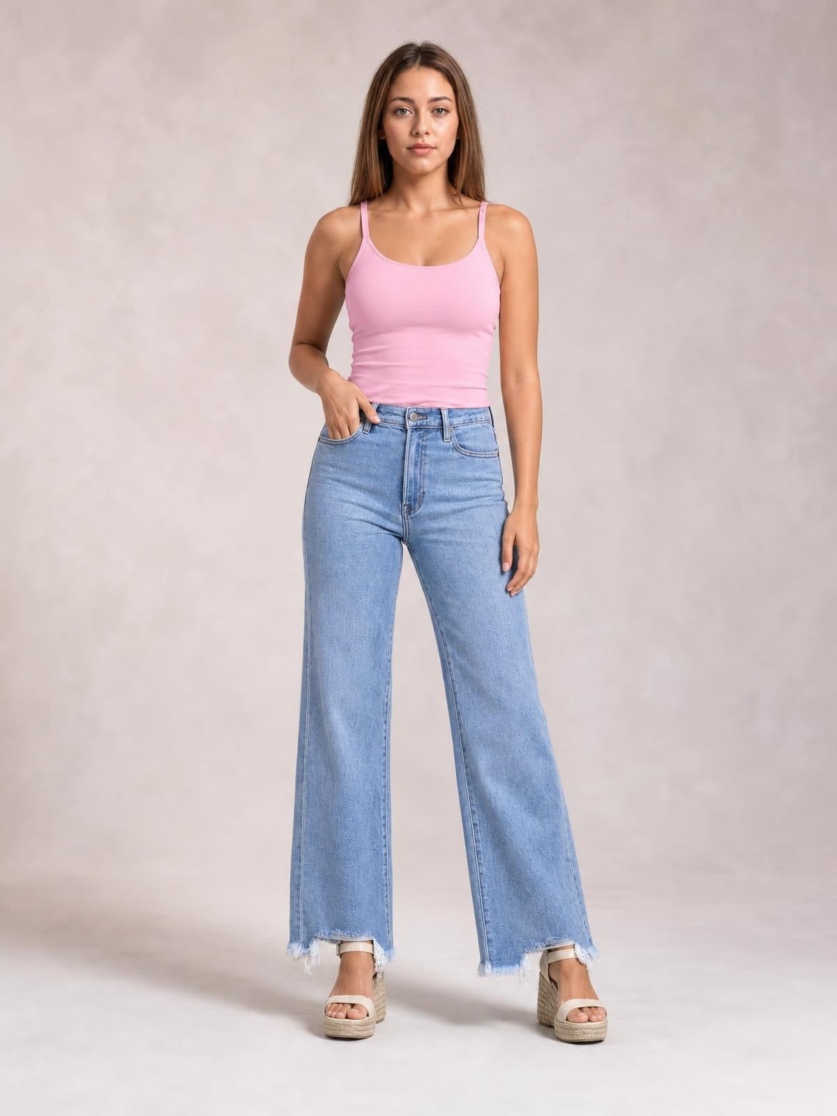 Model wearing light-wash loose-fit jeans with a button fly, front pockets, wide-leg silhouette, and frayed raw hems, standing with one hand in a pocket.