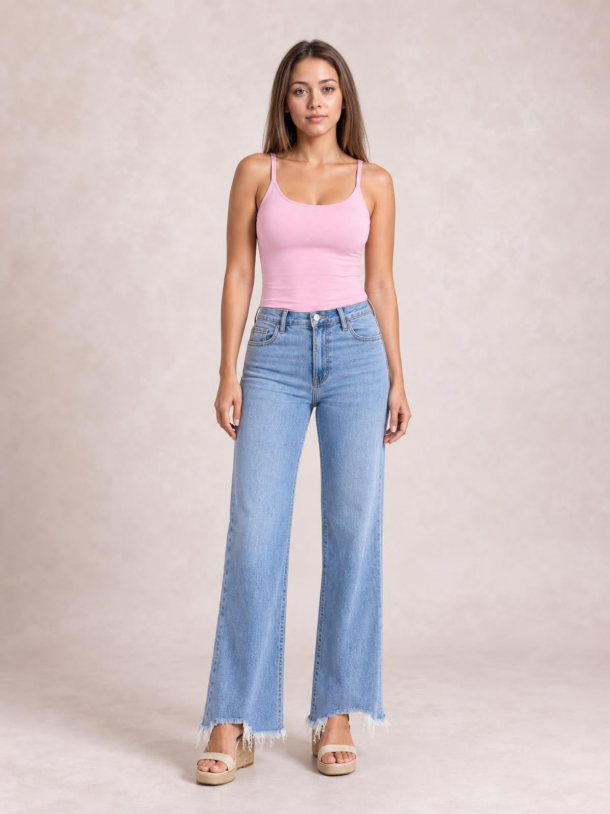 A model stands wearing light blue loose-fit jeans with a button closure, front pockets, wide-leg silhouette, and frayed raw hems.
