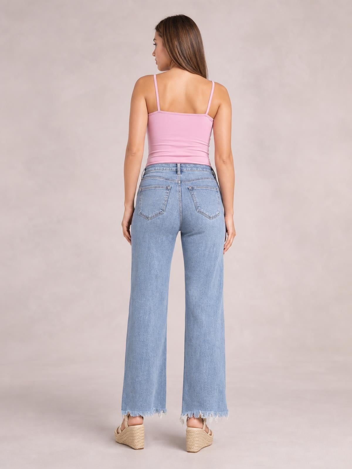 Model stands facing away in light blue raw hem loose fit jeans with a wide-leg silhouette, waistband belt loop, and two back patch pockets.