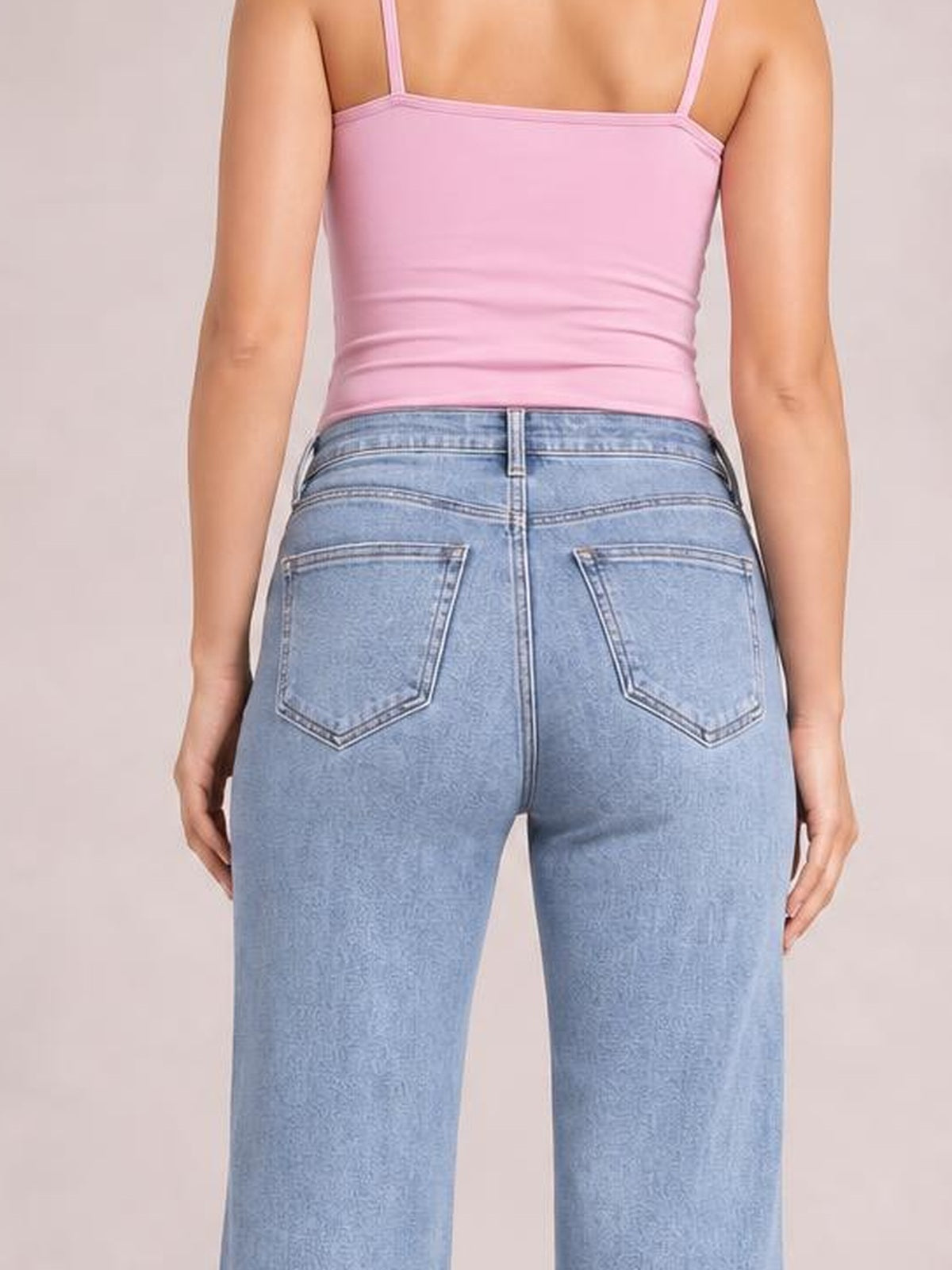 Rear view of a model wearing light blue loose fit jeans with a structured waistband, belt loops, contrast stitching, and two large back patch pockets.