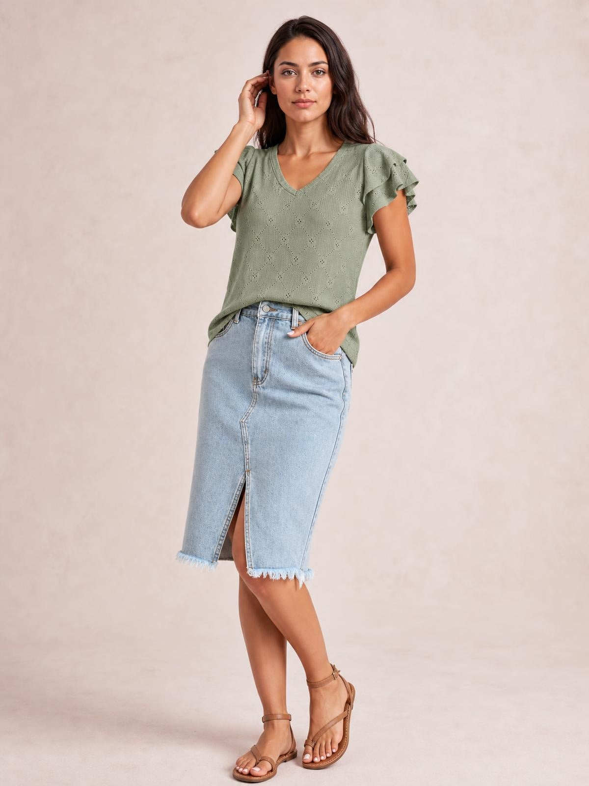 A model poses in a light blue raw hem denim midi skirt with button closure, pockets, a front slit, and a straight silhouette, one hand in a pocket.