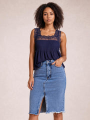 Model poses with one hand in the pocket of a light blue denim skirt featuring a button front, pencil silhouette, center slit, and raw hem.