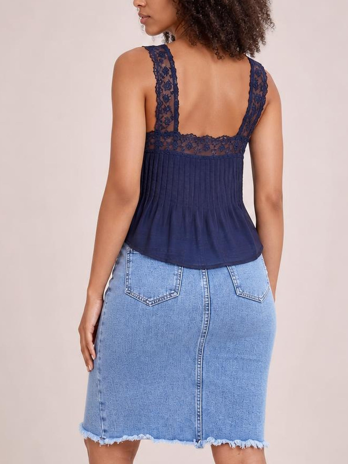 Model shown from the back wears a light-blue denim skirt with back pockets, fitted knee-length silhouette, center seam, and raw frayed hem.