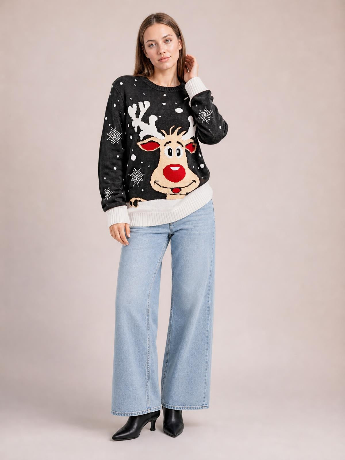 Model wears a black Reindeer round neck sweater with white ribbed cuffs and hem, festive reindeer and snowflake pattern, relaxed silhouette, and long sleeves.