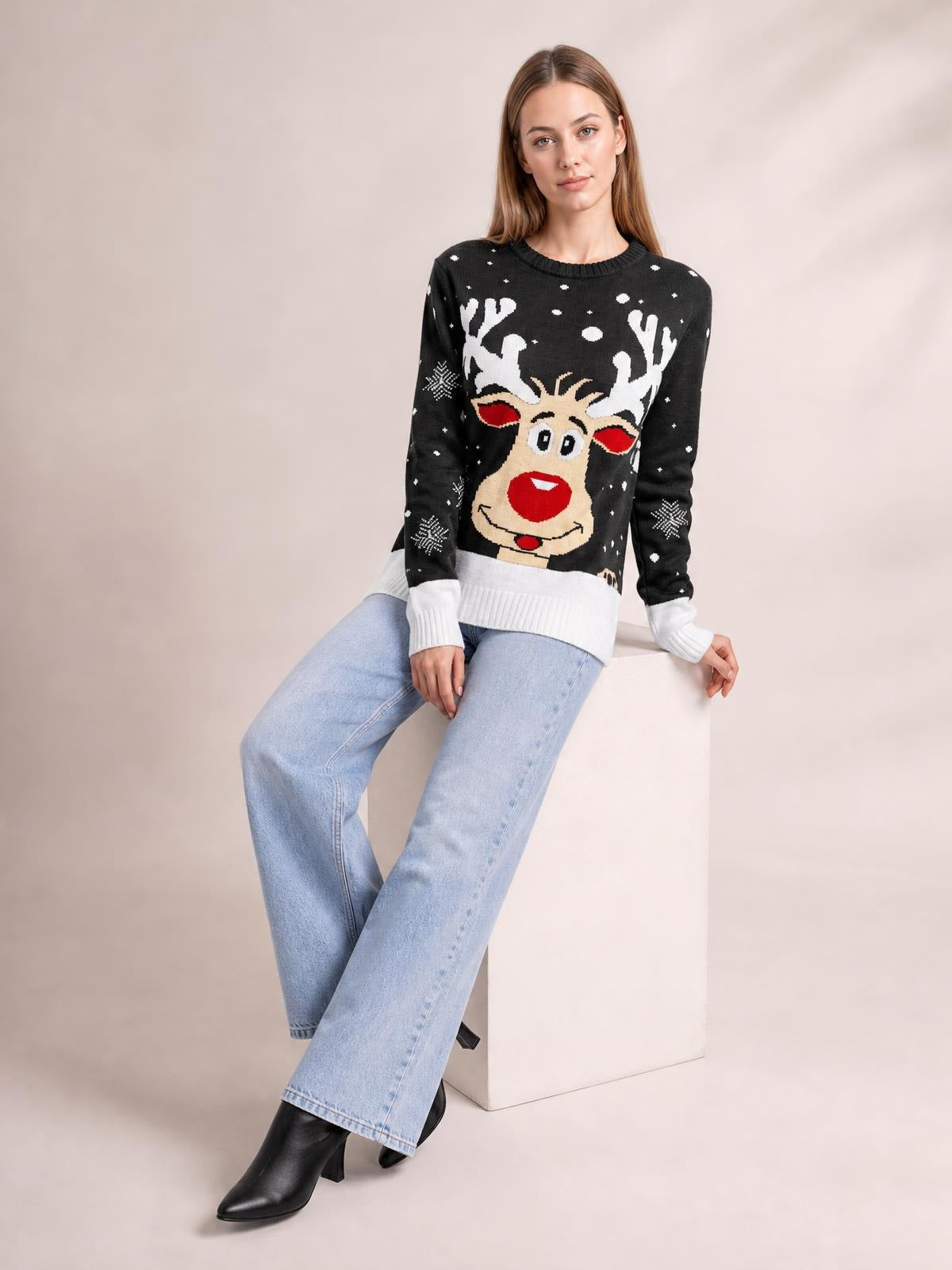 Model seated in a black Reindeer round neck sweater with a festive reindeer motif, white ribbed cuffs and hem, and a relaxed long-sleeve silhouette.