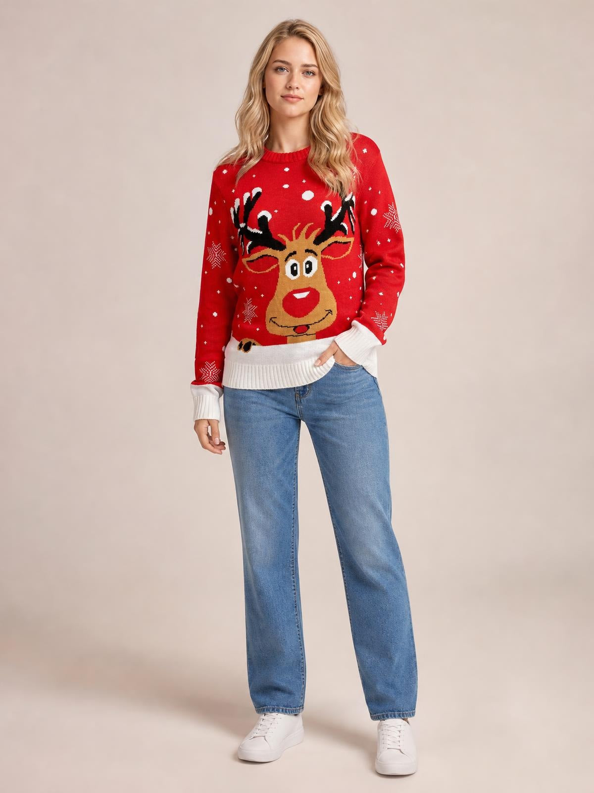 Model wearing a red reindeer round neck sweater with white ribbed cuffs and hem, snowflake accents, relaxed fit, and long sleeves, standing with one hand in a pocket.