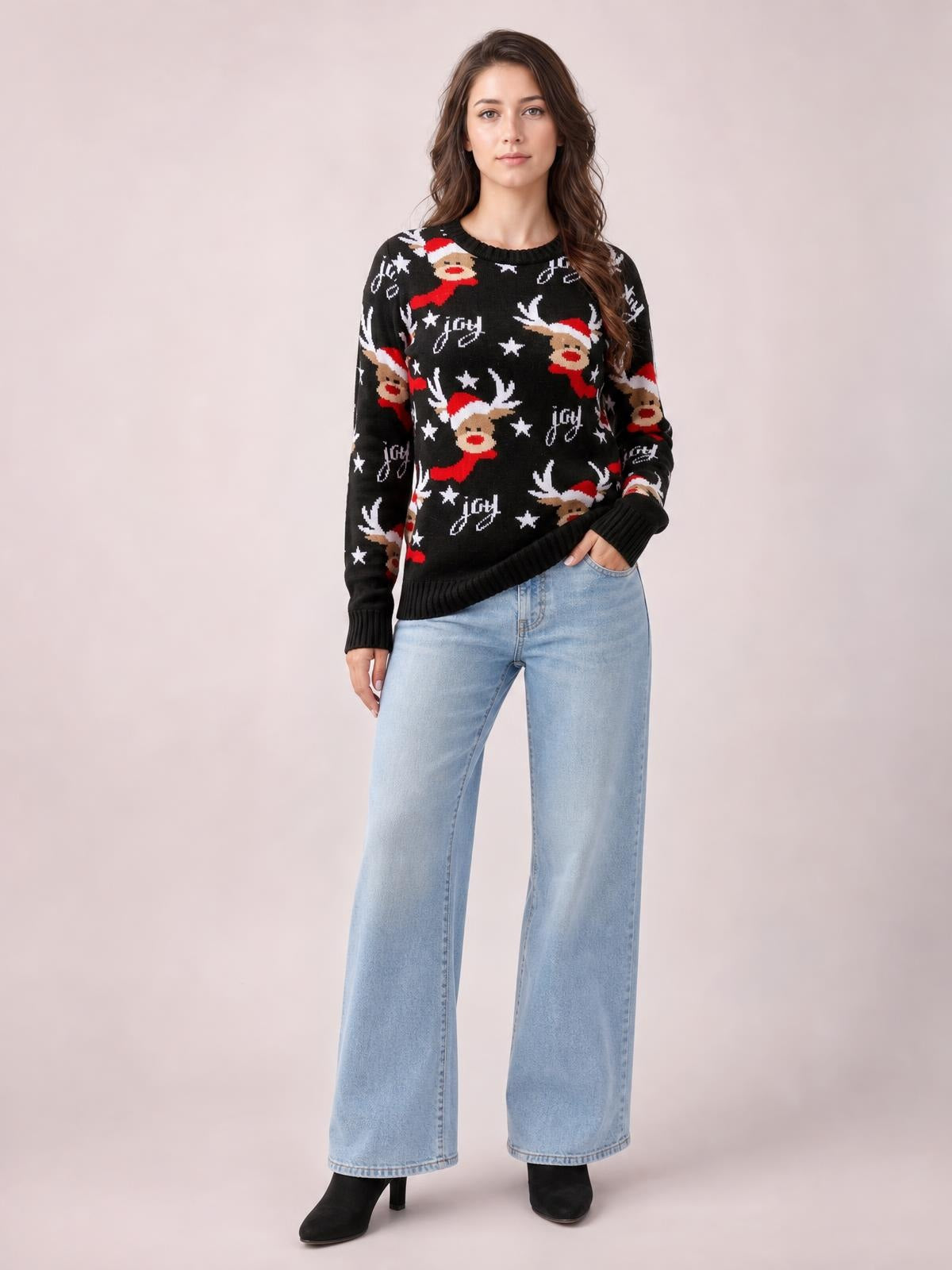 Model wearing a black round-neck Reindeer sweater with red, white, and tan festive motifs, long sleeves, ribbed cuffs and hem, shown in a relaxed standing pose.