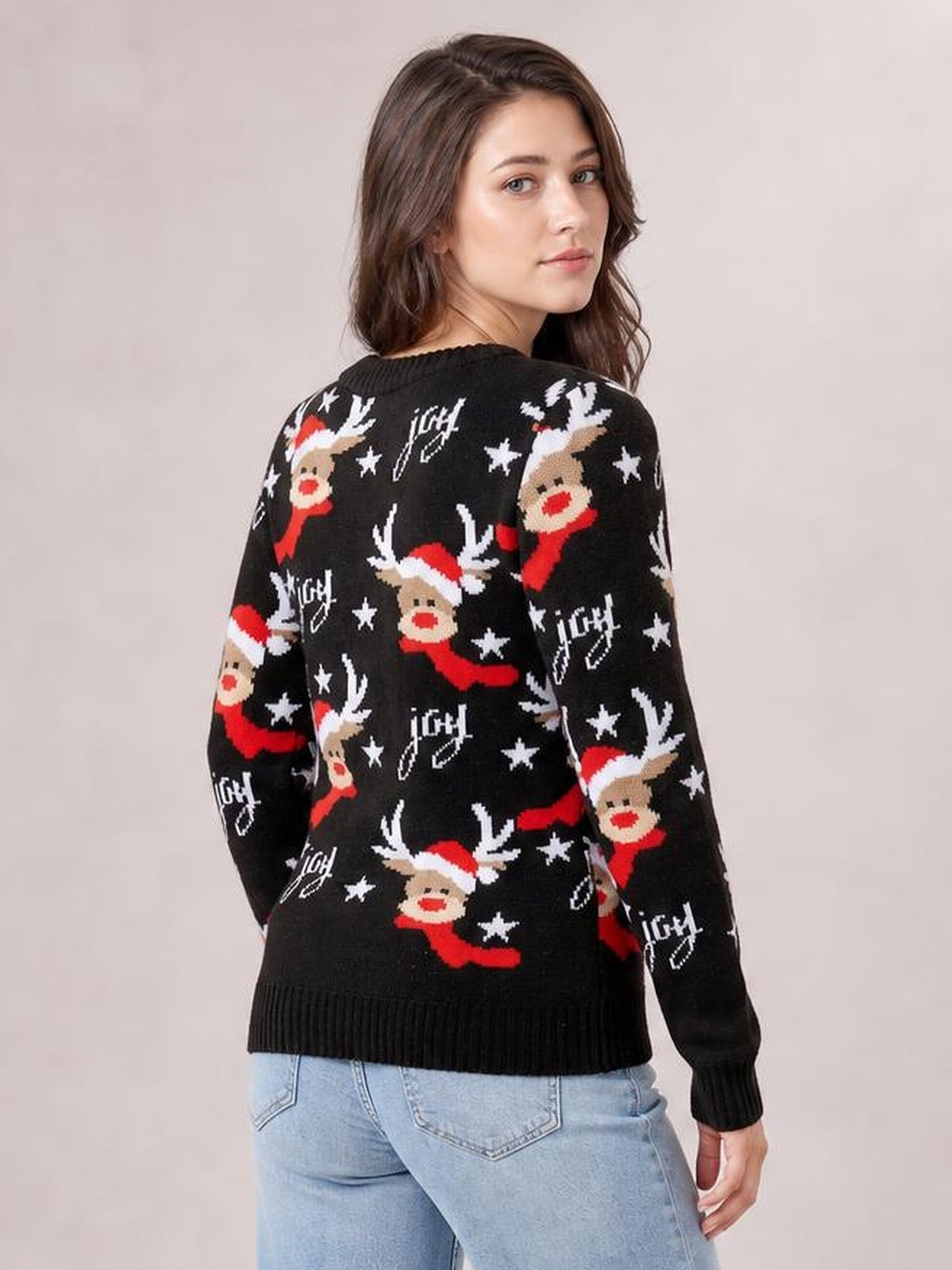 A model turns to show a black reindeer round neck sweater with long sleeves, festive red and white motifs, a relaxed silhouette, and ribbed cuffs and hem.