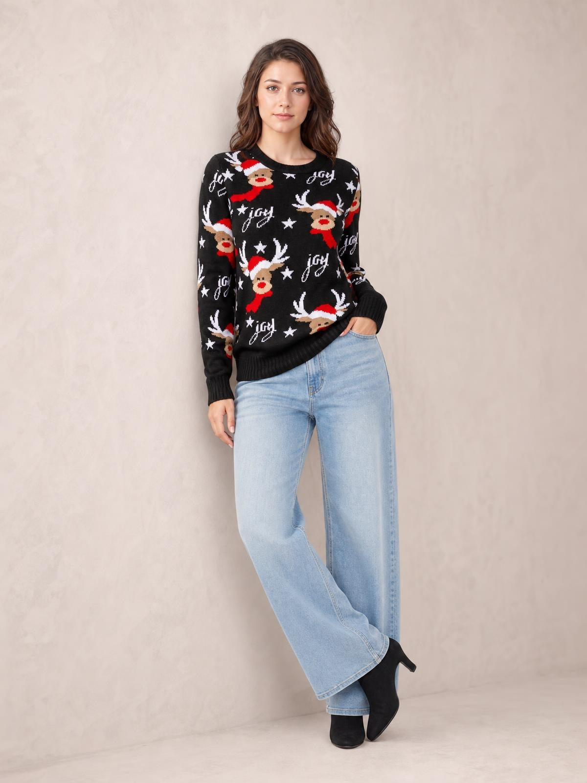 Model poses in a black round neck reindeer sweater with long sleeves, ribbed cuffs and hem, a relaxed silhouette, and festive red, white, and tan motifs.