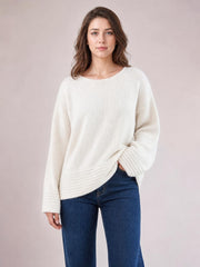 Model wears a relaxed-fit ivory round-neck sweater with long sleeves, ribbed cuffs and hem, a loose silhouette, and one hand resting at the hip.