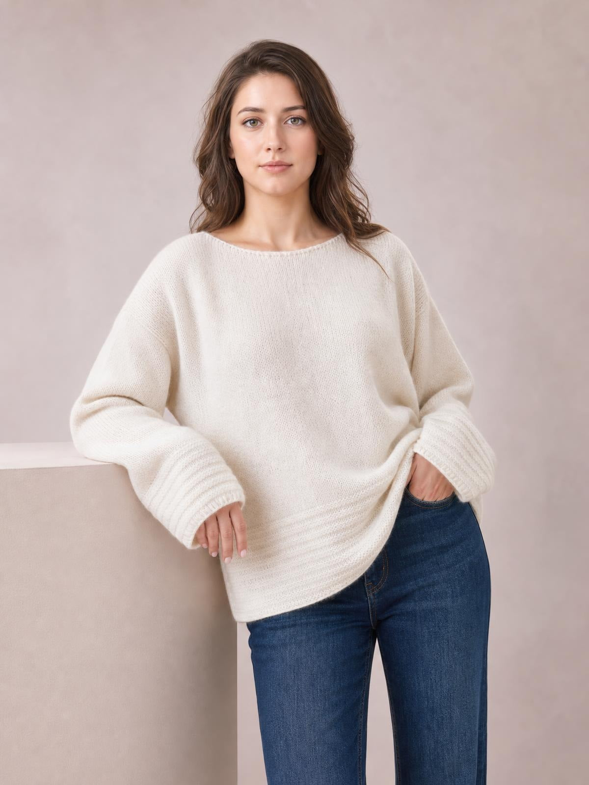 Model wearing a cream relaxed-fit round-neck sweater with a soft knit texture, dropped shoulders, long sleeves, ribbed cuffs and hem, posed with one hand in a jeans pocket.