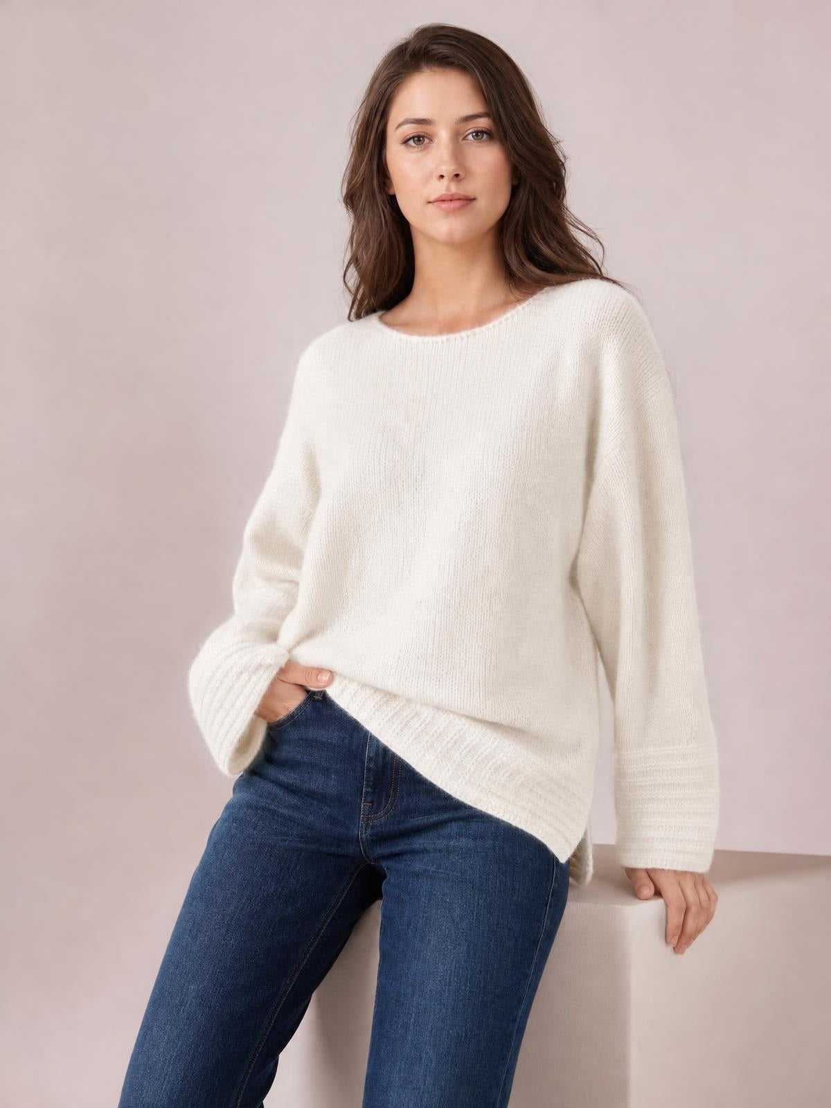 Model seated in a relaxed pose wearing an ivory relaxed-fit round neck sweater with long sleeves, ribbed cuffs and hem, and a soft knit silhouette.