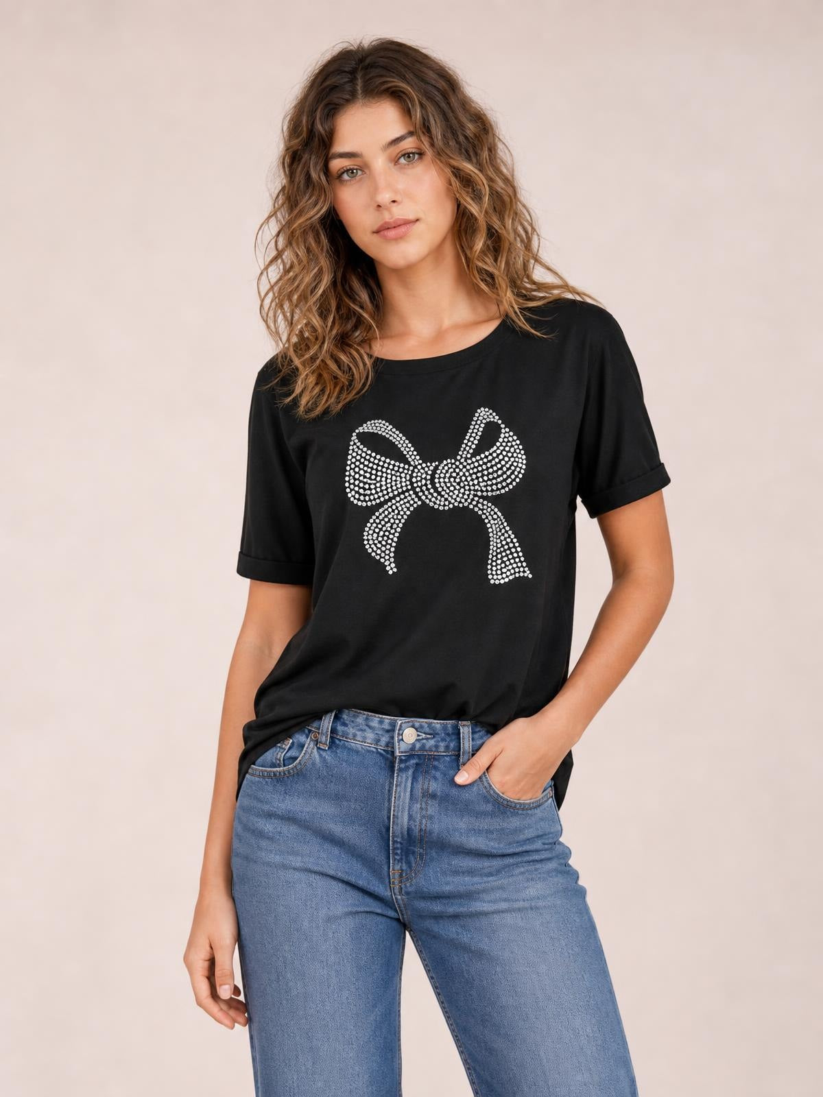 Model poses in a black round-neck short-sleeve T-shirt with rolled cuffs, a relaxed silhouette, and a sparkling rhinestone bow graphic.
