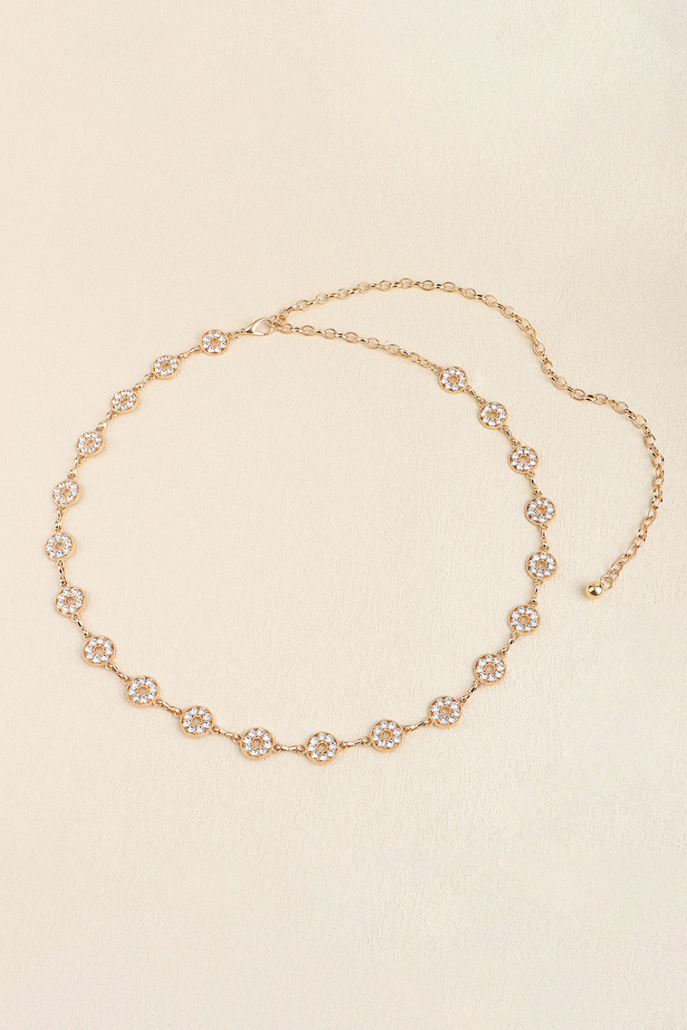 Slim gold-tone zinc alloy belt with linked chain construction and a succession of sparkling circular rhinestone accents for an elegant, jewelry-inspired drape.