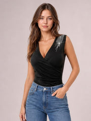 Model poses in a fitted black surplice tank with a V-neckline, wide shoulder straps, rhinestone accents, and a ruched waist, one hand in her jeans pocket.