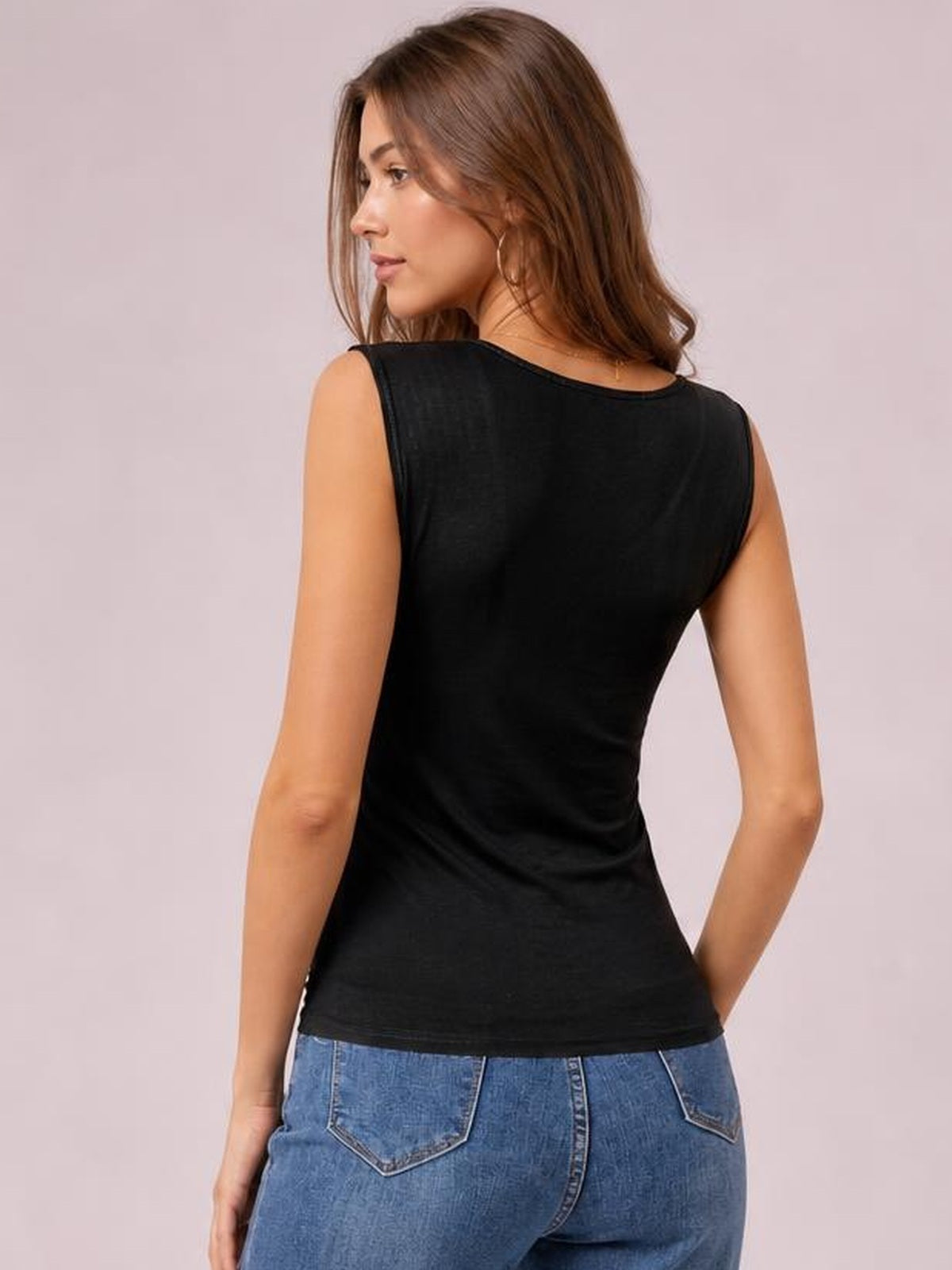 A model turns slightly to show a black sleeveless tank with a smooth, fitted silhouette, wide shoulder straps, and a straight hem.