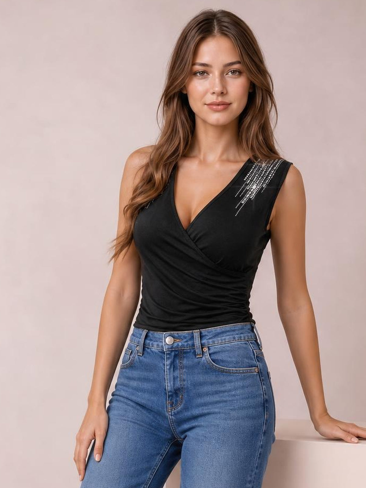 Model poses in a fitted black surplice tank with a V-neck, ruched waist, wide shoulder straps, and sparkling rhinestone detail near the right shoulder.
