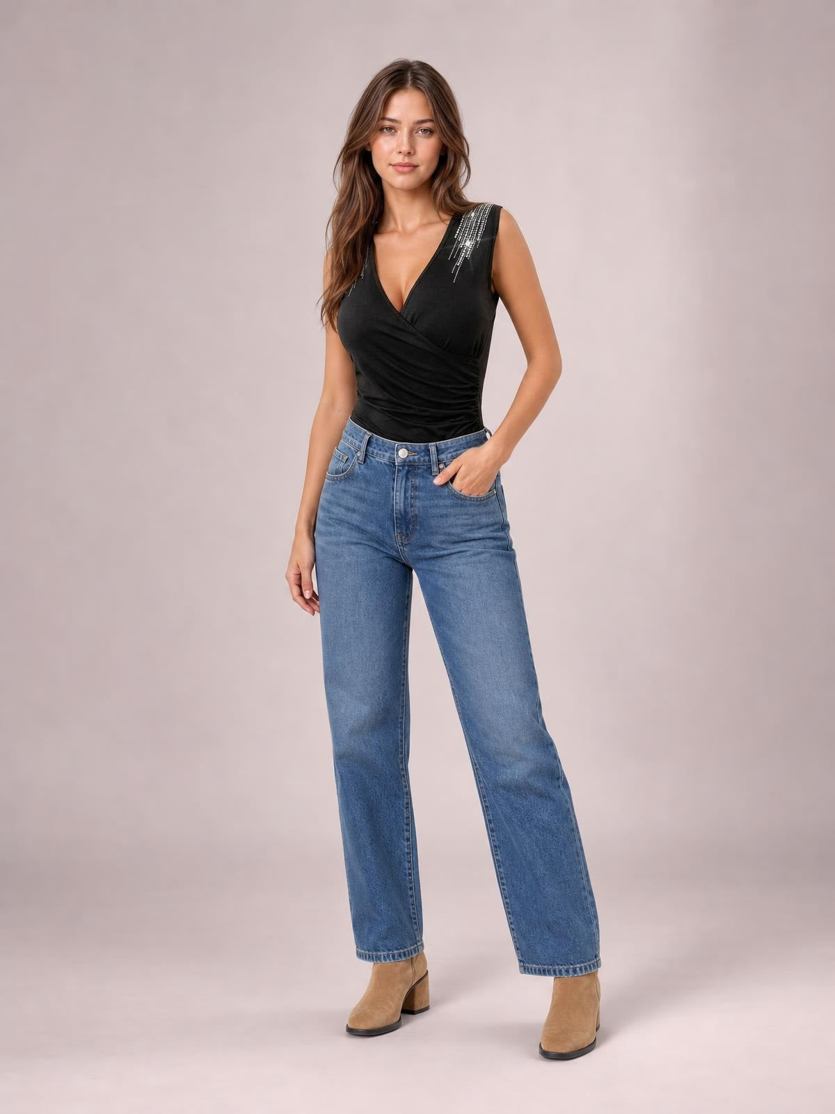 A model poses with one hand in her jeans pocket, wearing a black sleeveless surplice tank with a ruched fitted silhouette and rhinestone shoulder detail.