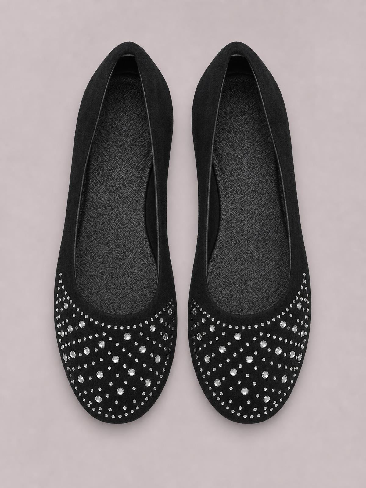 Black flat slip-on shoes feature rounded toes, low-cut uppers, and rows of sparkling rhinestones across the vamp on a smooth PU leather design.