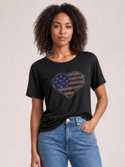 Model wears a black rhinestone heart round-neck short-sleeve T-shirt with a relaxed silhouette, standing front-facing with one hand in her jeans pocket.