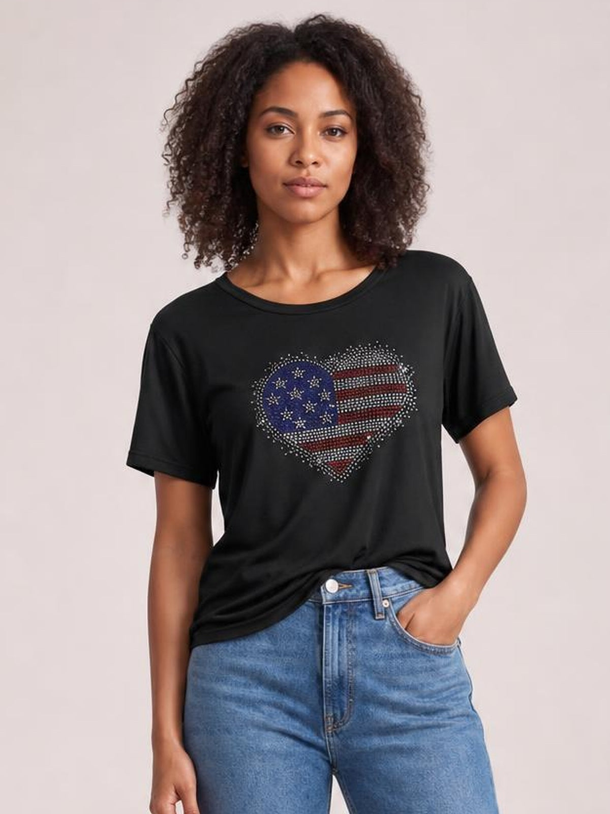 Model wears a black rhinestone heart round-neck short-sleeve T-shirt with a relaxed silhouette, standing front-facing with one hand in her jeans pocket.