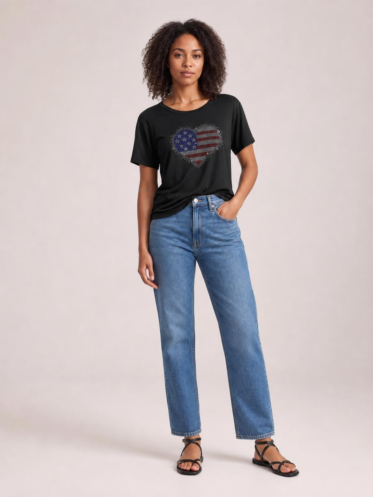 Model stands in a black round-neck short-sleeve T-shirt with a sparkling rhinestone heart graphic and relaxed silhouette, one hand in her jeans pocket.