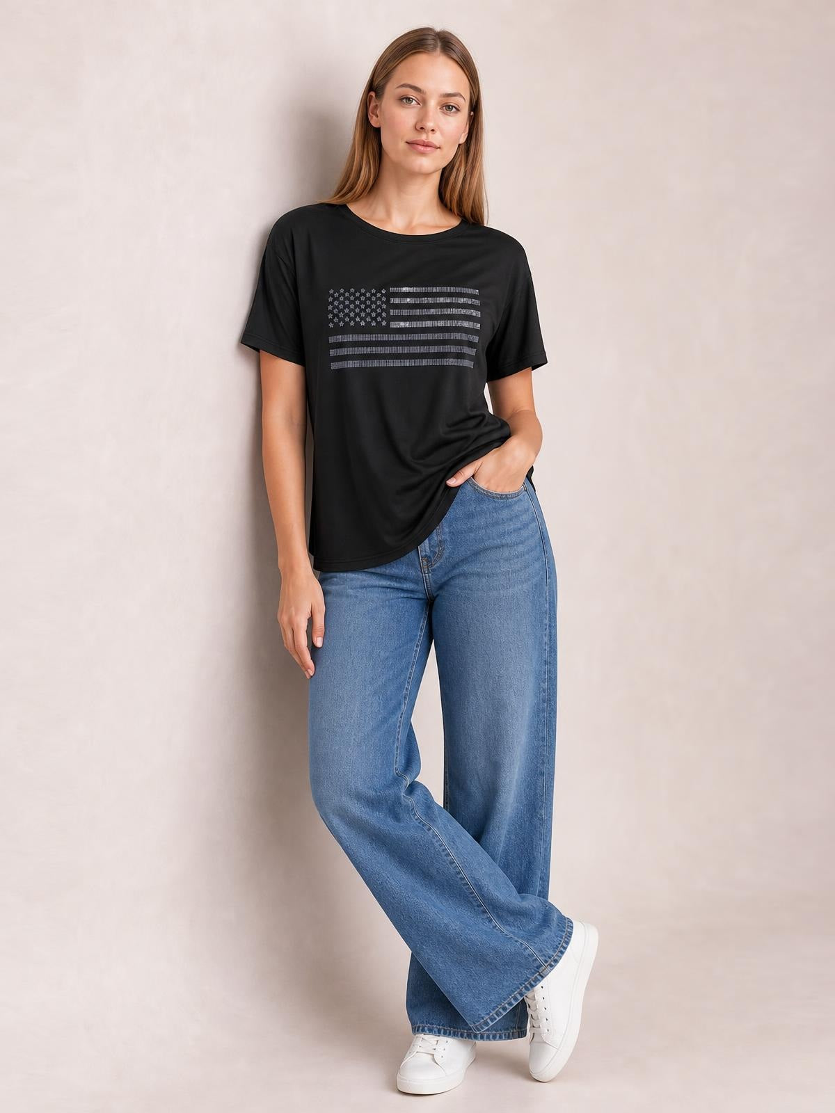 Model poses in a black round-neck short-sleeve T-shirt with a rhinestone US flag graphic, relaxed silhouette, and one hand in her jeans pocket.