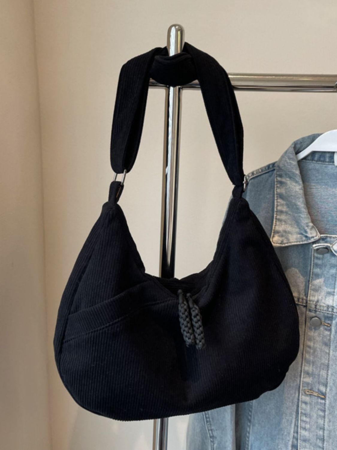 A large black ribbed shoulder bag hangs from a wide adjustable strap, featuring a softly curved slouchy silhouette and braided pull detail.