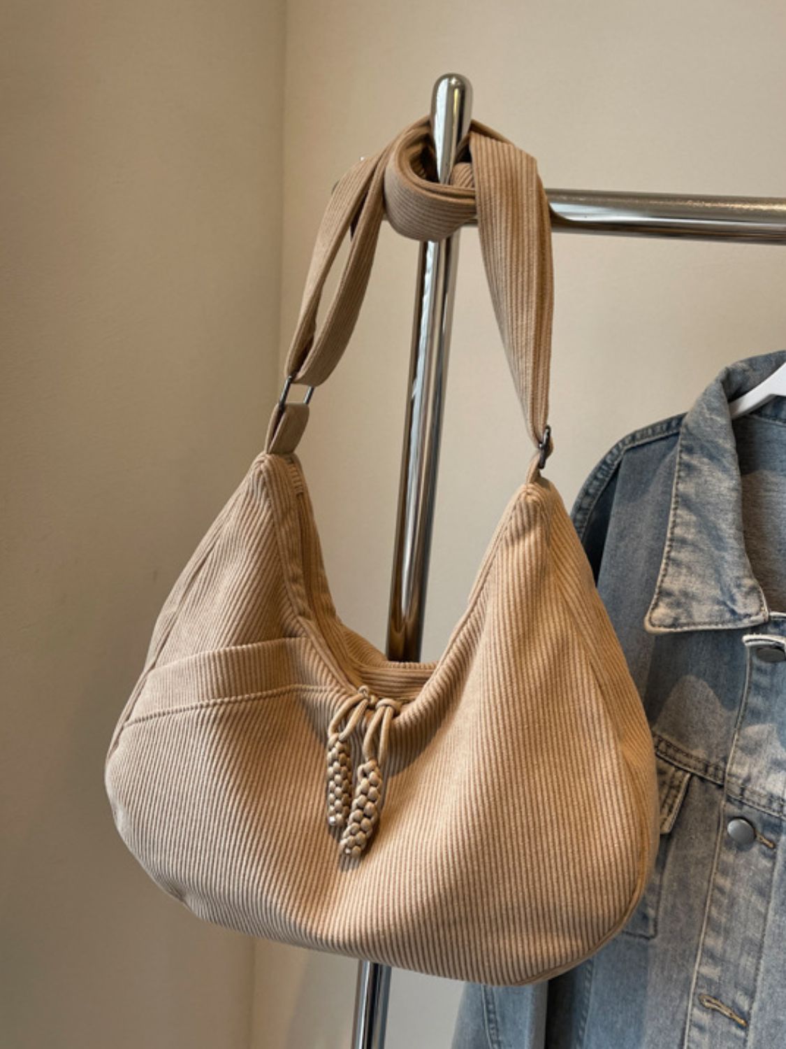 Large beige ribbed shoulder bag with a softly curved, slouchy silhouette, adjustable strap, gathered opening, and decorative braided pulls.