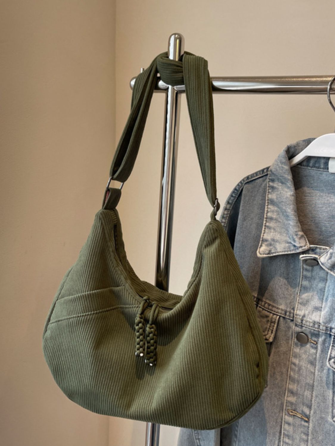 Large olive-green ribbed shoulder bag with a softly slouchy silhouette, adjustable strap, gathered construction, and decorative braided zipper pulls.