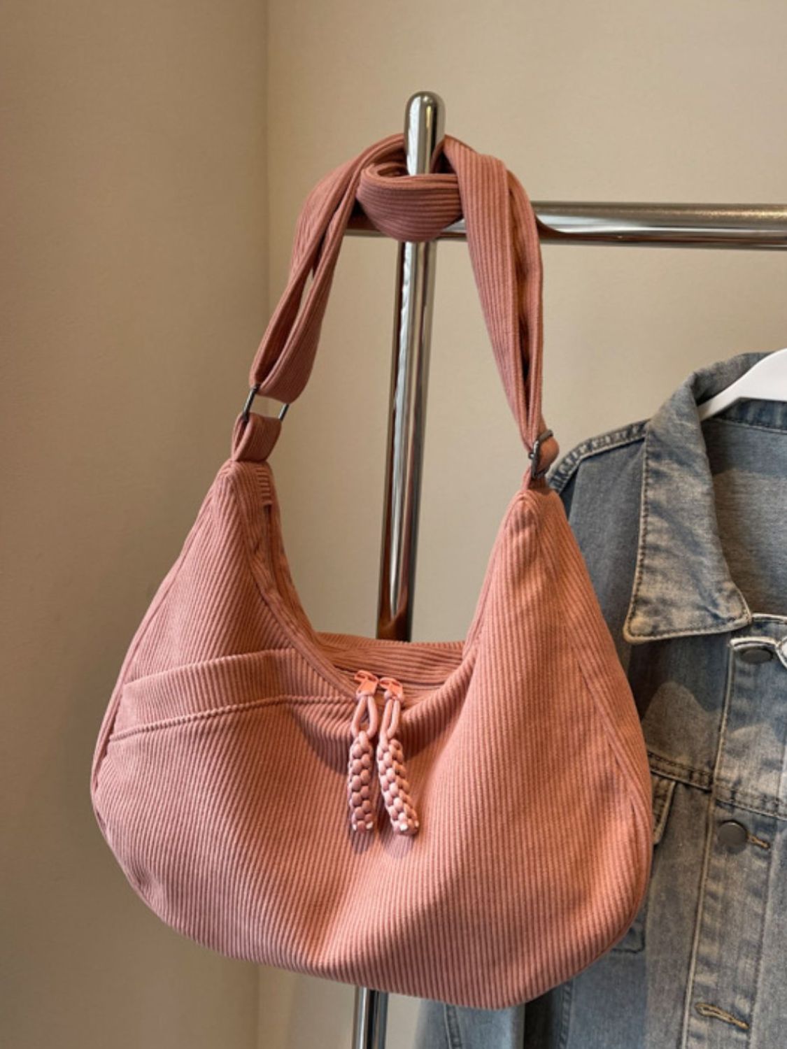 Large pink ribbed shoulder bag with a softly curved, slouchy silhouette, adjustable strap, zip-top closure, and decorative braided pulls.