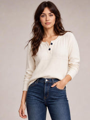 Model in a relaxed pose wears an ivory ribbed sweater with a round neckline, button detail, seam detail, long sleeves, and a loose silhouette.