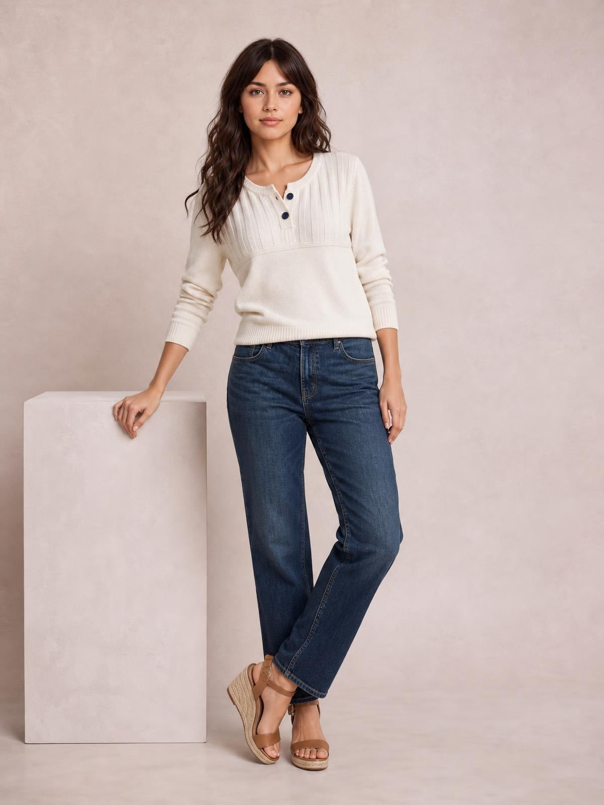 Model poses in a cream ribbed sweater with buttoned neckline, seam detail, long sleeves, and a relaxed silhouette.