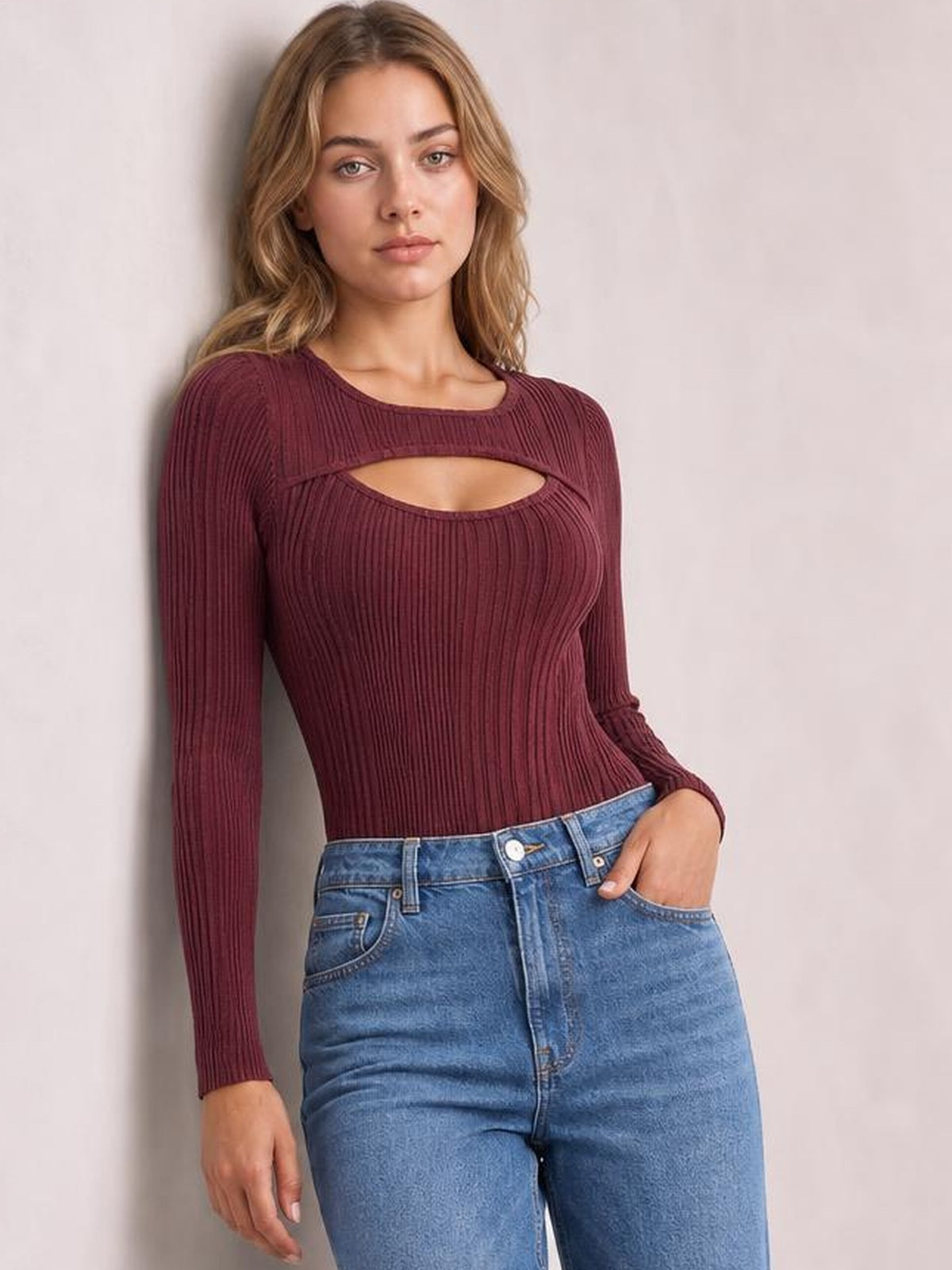 Model poses with one hand in her jeans pocket wearing a burgundy ribbed bodysuit with a round neck, long sleeves, chest cutout, and fitted silhouette.