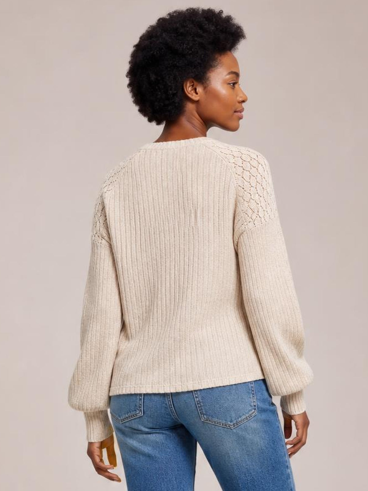 A model looks over her shoulder wearing a cream ribbed round-neck long-sleeve top with textured shoulder panels and a straight, fitted silhouette.