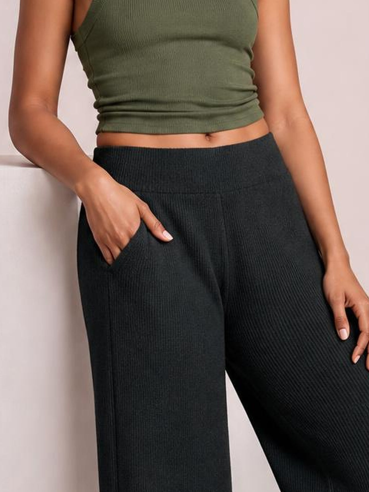 A model wears black ribbed wide-leg pants with a comfortable waistband and side pocket, posing with one hand tucked into the pocket.