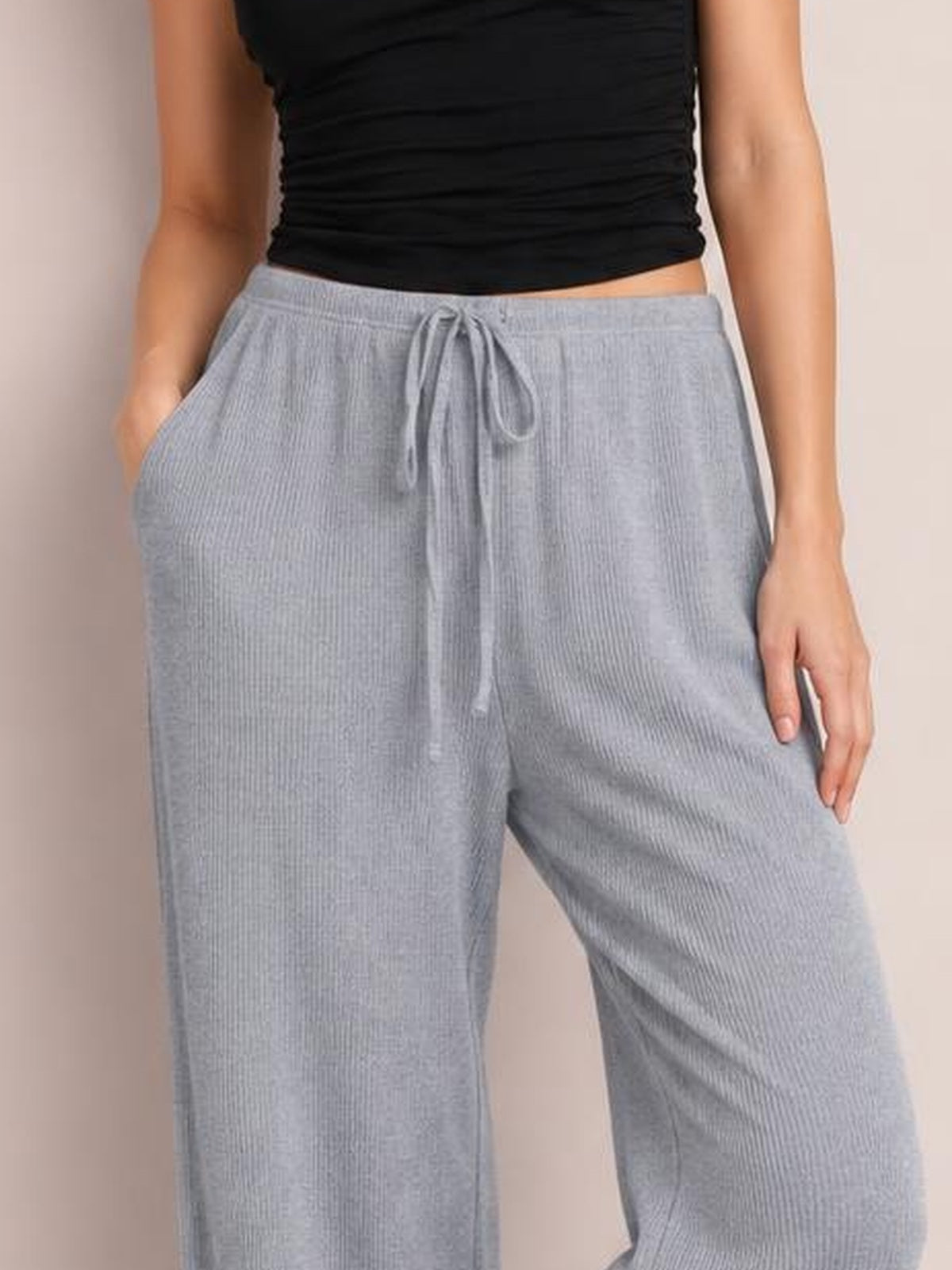 Model wears light gray ribbed drawstring wide leg pants with an elastic waist, side pockets, and a relaxed silhouette.