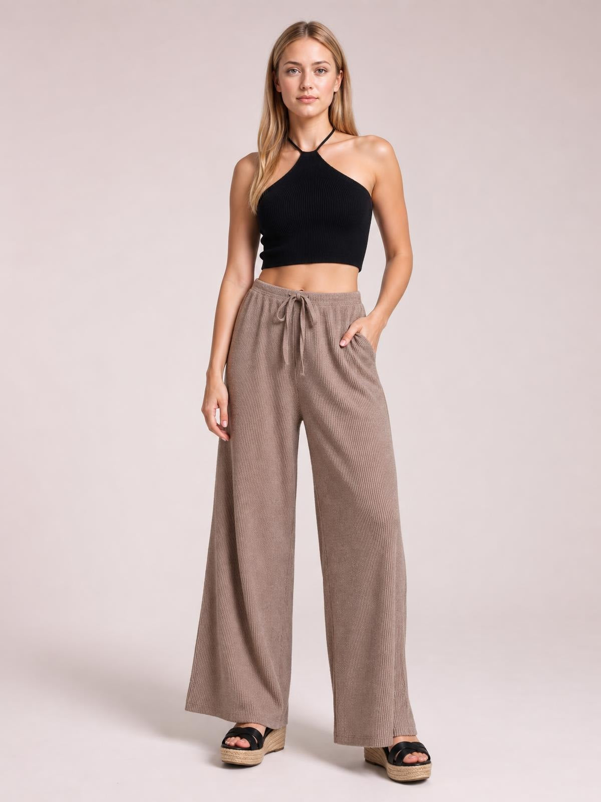 A model stands in taupe ribbed drawstring wide-leg pants with a relaxed silhouette, elastic waistband, and visible side pockets.