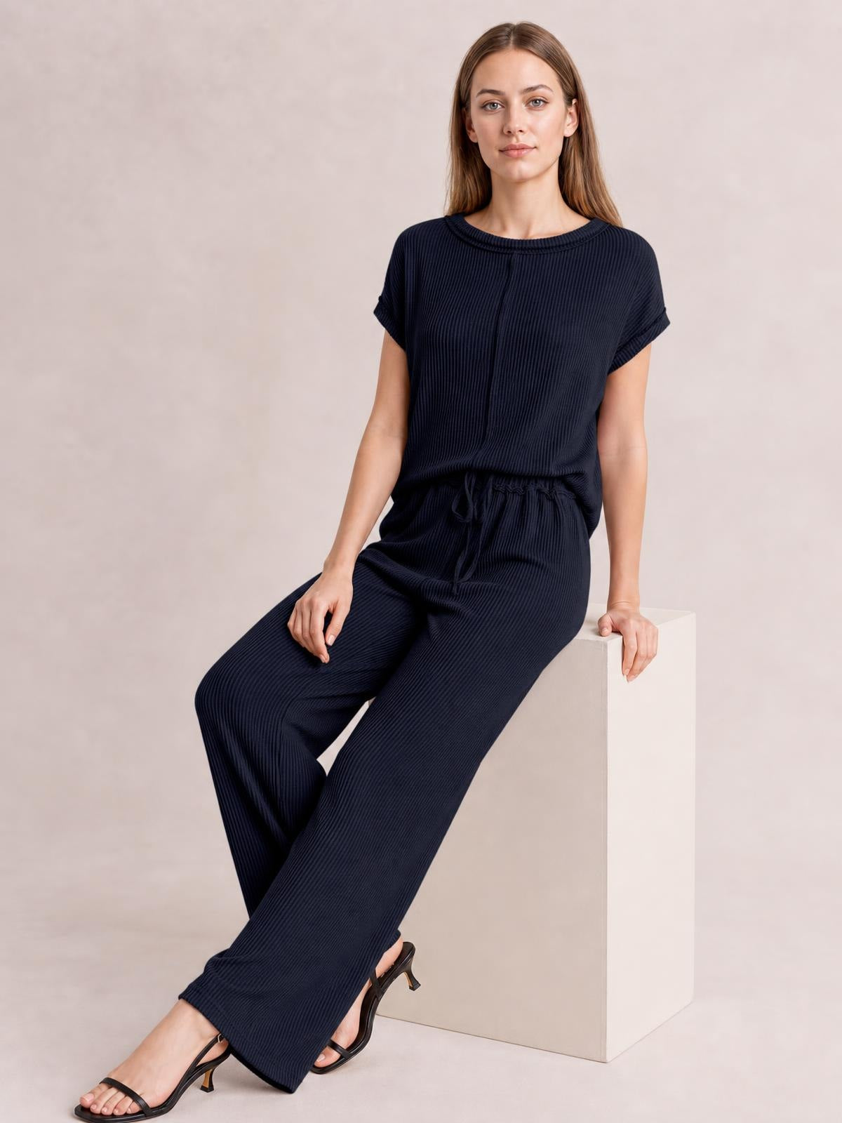 A model sits in a dark navy ribbed exposed seam top and pants set, featuring a relaxed short-sleeve top and wide-leg pants with a drawstring waist.