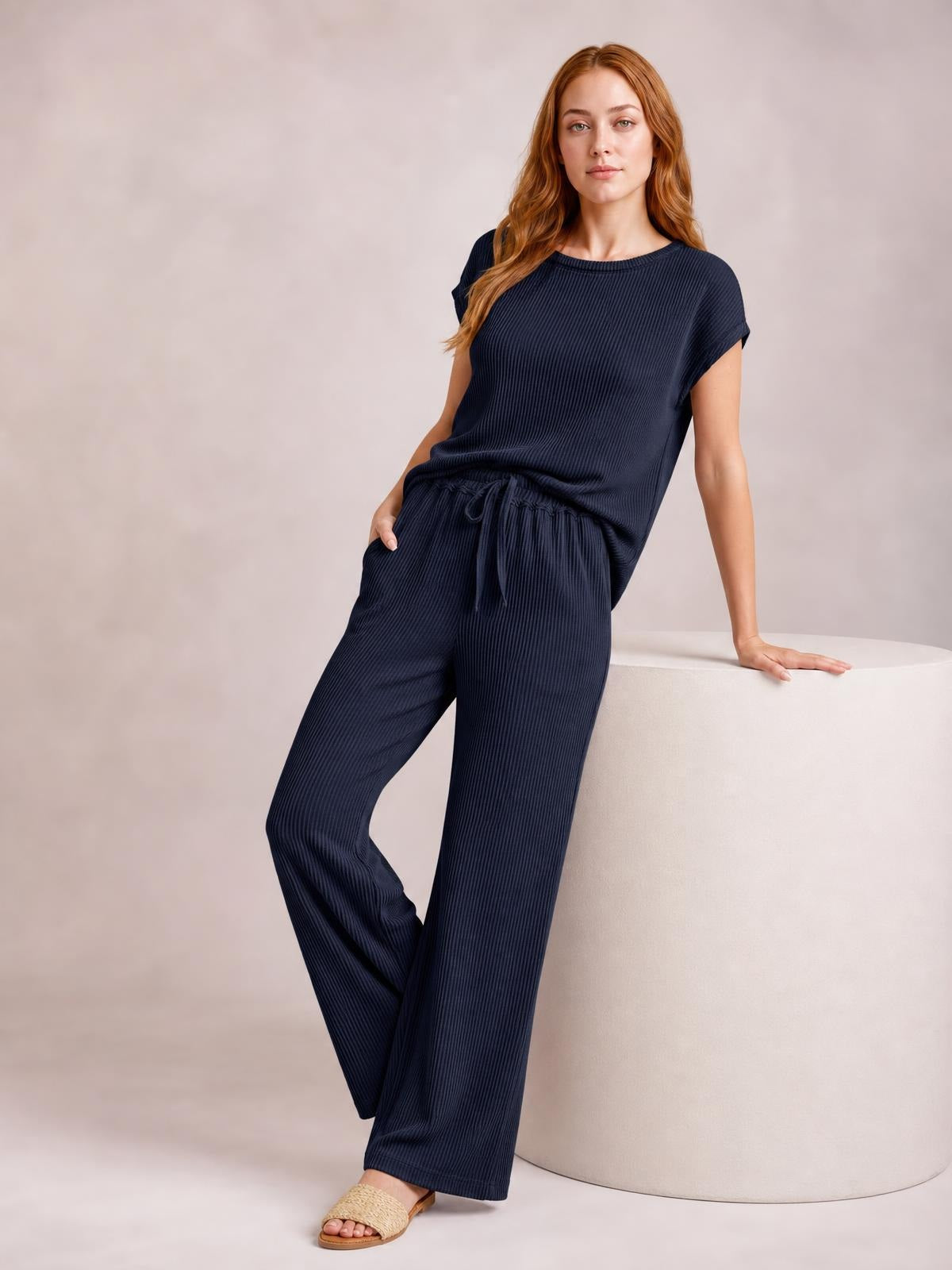 Model leans against a ledge wearing a navy ribbed top and wide-leg pants set with exposed seams, short sleeves, and a drawstring waist.