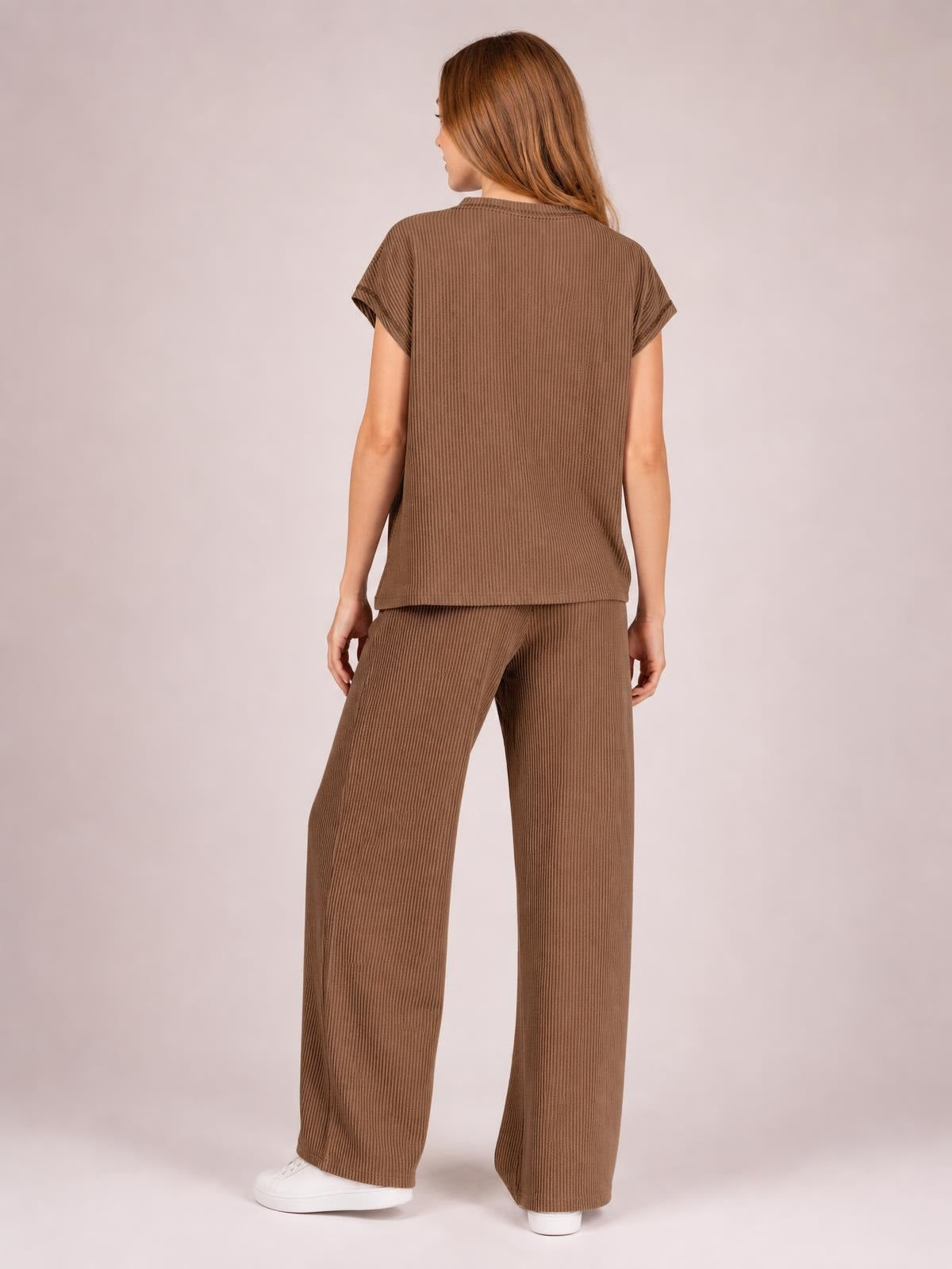 A model stands in a brown ribbed exposed seam top and pants set, showing the short-sleeve top and relaxed wide-leg silhouette from the back.